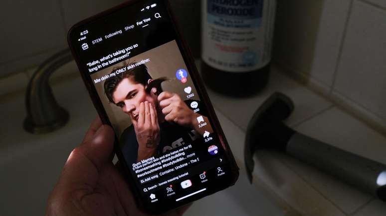 Imagem ilustrativa do movimento looksmaxxing, reproduzindo v&iacute;deo no TikTok de influenciador martelando a ma&ccedil;&atilde; de seu rosto para parecer mais masculino