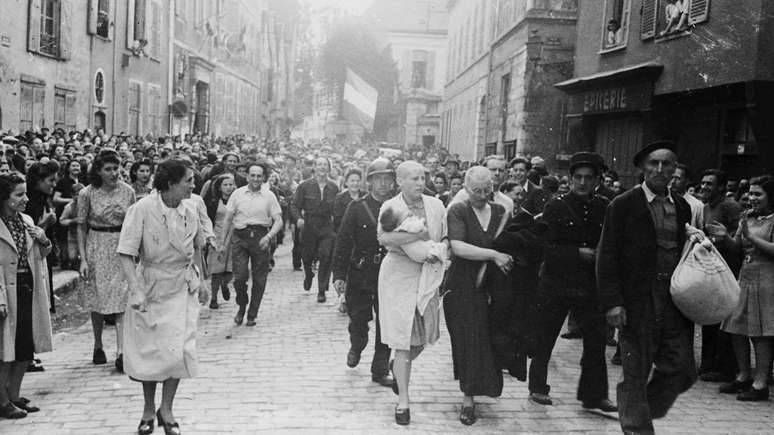 Na fotografia de Robert Capa, uma jovem m&atilde;e com a cabe&ccedil;a raspada como forma de puni&ccedil;&atilde;o &eacute; conduzida por uma multid&atilde;o