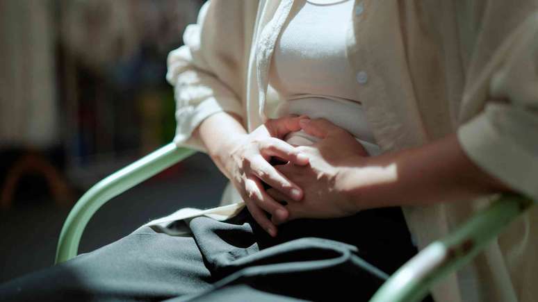 Pessoa sentada em uma cadeira, com as m&atilde;os pressionadas contra o abd&ocirc;men