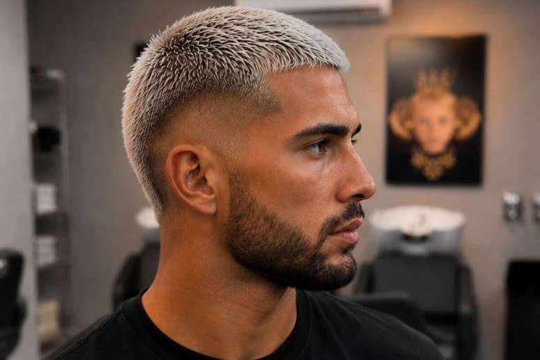 Homem com corte militar e cabelo platinado, rosto s&eacute;rio e olhando para o lado