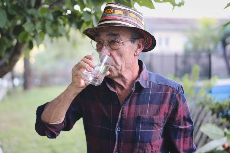 Homem, usando camisa xadrez e chap&eacute;u, bebendo &aacute;gua