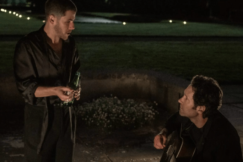 Dois homens conversando durante a noite, enquanto um deles toca viol&atilde;o