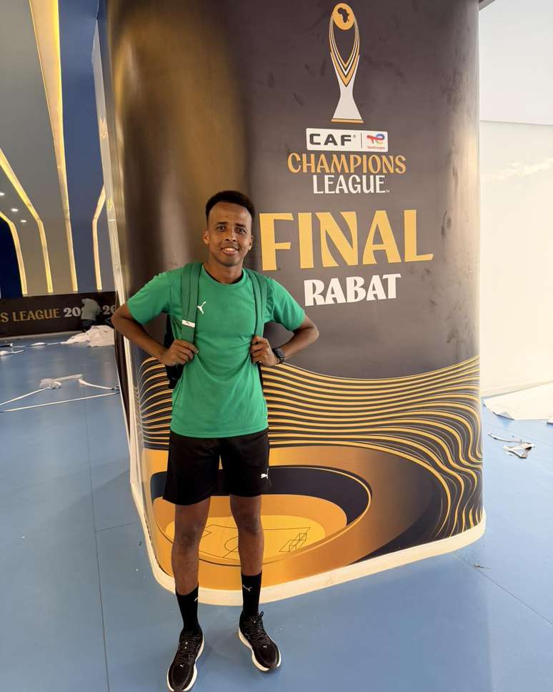 Omar Artan, &aacute;rbitro somali, posando ao lado de banner da final da Liga dos Campe&otilde;es da CAF &ndash; 