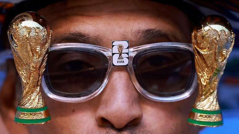 Uma foto em close-up de um homem usando &oacute;culos escuros com uma miniatura da Copa do Mundo em cada lado.