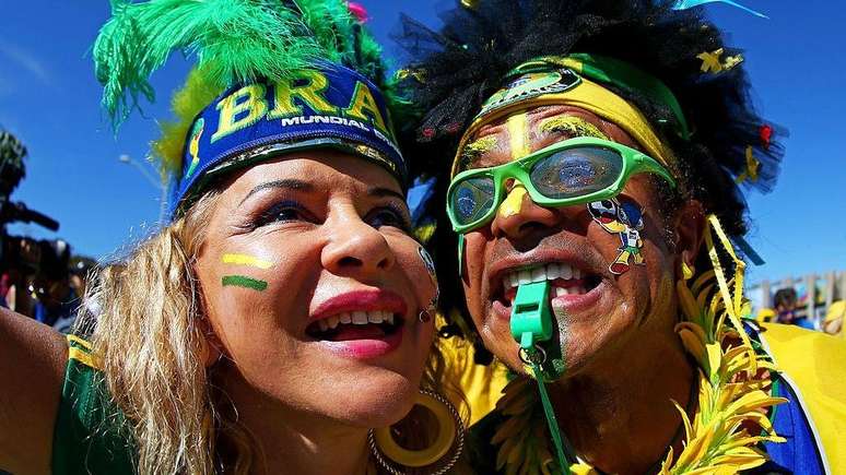Uma foto em close-up de dois torcedores brasileiros vestindo roupas verdes e amarelas, al&eacute;m de cocares de penas.