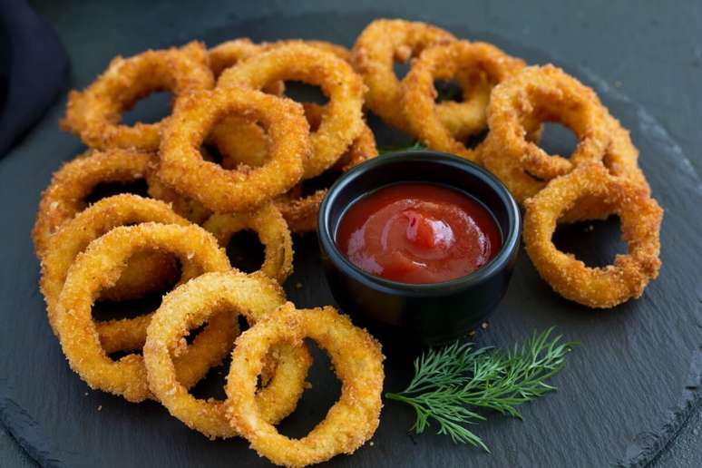 Onion rings servida em bancada de cer&acirc;mica com pote com ketchup ao lado