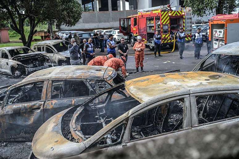 Bombeiros e policiais trabalham ao lado de ve&iacute;culos incendiados no local da queda de helic&oacute;pteros no bairro do Recreio dos Bandeirantes