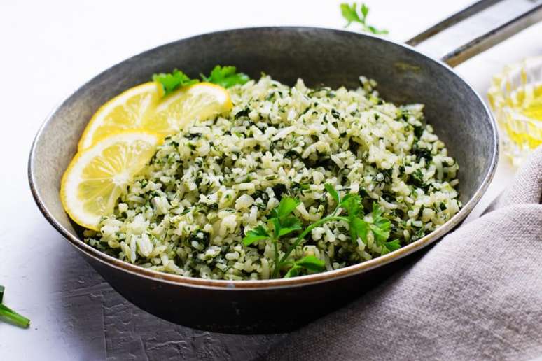A imagem mostra um prato de arroz verde preparado com folhas picadas misturadas aos gr&atilde;os, decorado com fatias de lim&atilde;o e salsinha fresca. Pela apar&ecirc;ncia, trata-se de um arroz com ora-pro-n&oacute;bis