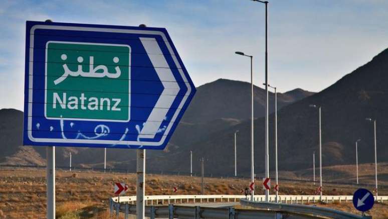Uma placa de tr&acirc;nsito azul e verde que diz &ldquo;Natanz&rdquo; no Ir&atilde; fica ao lado de uma rodovia, com uma cordilheira ao fundo