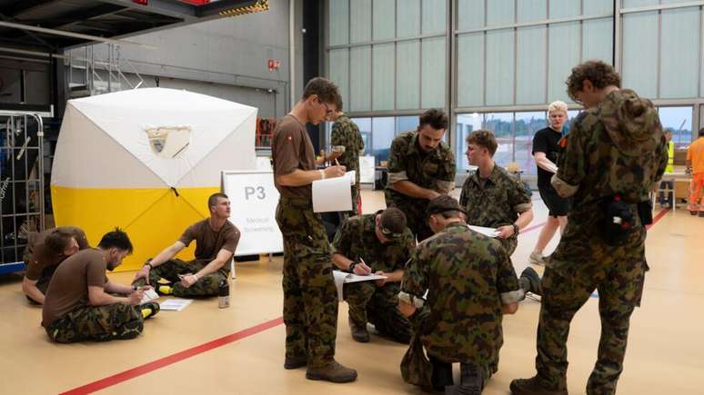 Militares su&iacute;&ccedil;os assinam documentos no Aeroporto de Zurique antes de embarcar para a Venezuela para atuar na resposta aos terremotos. 25 de junho de 2026