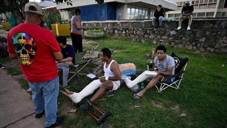 Pessoas feridas com as pernas engessadas permanecem no lado externo do hospital Domingo Luciani de Caracas, no dia 25 de junho de 2026, ap&oacute;s os dois terremotos que sacudiram a capital venezuelana