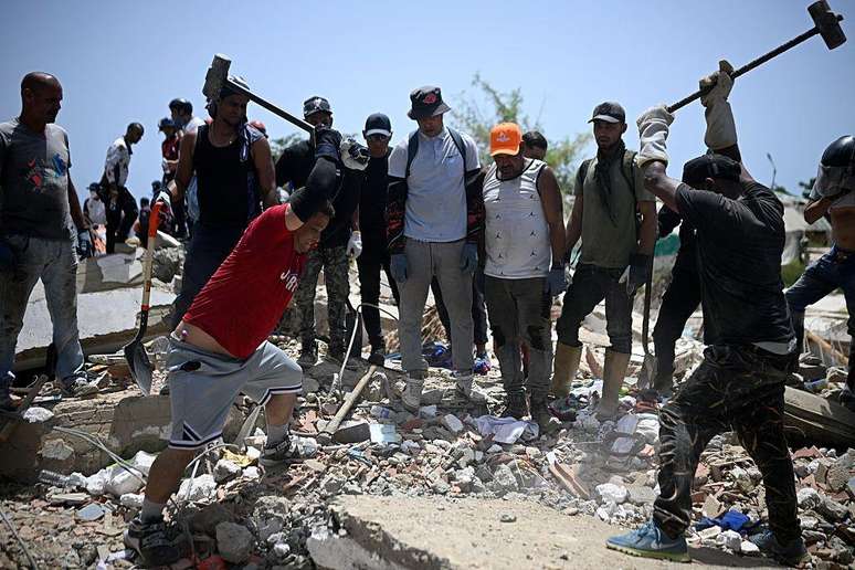 Volunt&aacute;rios golpeiam restos de concreto com marretas de ferro em busca de sobreviventes sob os escombros em La Guaira, Venezuela, 26 de junho de 2026.