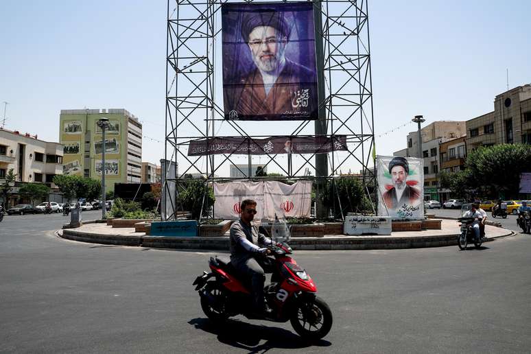 Pessoas passam de motocicleta por um banner com a foto do L&iacute;der Supremo do Ir&atilde;, Mojtaba Khamenei, em Teer&atilde;, Ir&atilde;, em 28 de junho de 2026