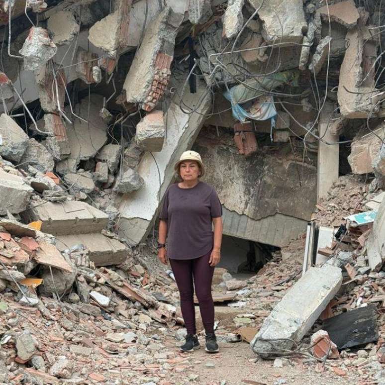 Mar&iacute;a Lourdes P&eacute;rez, vestida com cal&ccedil;a e camisa marrom e gorro bege, em frente a uma montanha de escombros, cimento, pedras e partes de uma edifica&ccedil;&atilde;o