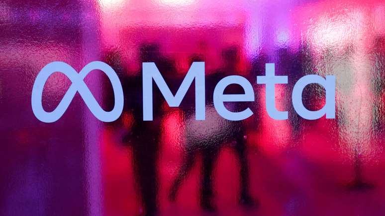 Logotipo da Meta exibido contra vidro fosco rosa e silhuetas de pessoas atr&aacute;s do logo