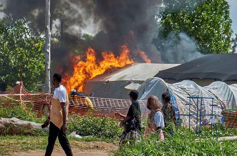 Pessoas passam por um centro de tratamento de ebola em chamas no hospital geral de Rwampara, em Bunia, ap&oacute;s um ataque
