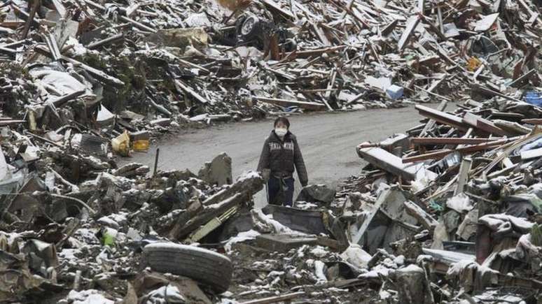 Uma mulher caminha entre os escombros na cidade japonesa de Minamisanriku, no norte do Jap&atilde;o, ap&oacute;s o tsunami de 2011.

