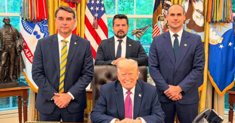 Foto do senador Fl&aacute;vio Bolsonaro, Donald Trump (sentado), Eduardo Bolsonaro (do lado direito) e Paulo Figueiredo sentado atr&aacute;s de Trump. Todos no sal&atilde;o oval da Casa Branca. 