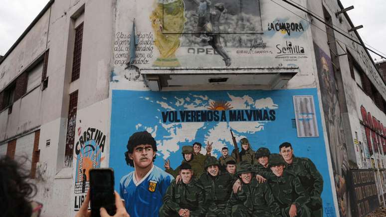 Uma pessoa fotografa um mural que retrata o astro do futebol Diego Maradona e veteranos da guerra de 1982 entre a Argentina e o Reino Unido, em Buenos Aires, na Argentina, na quarta-feira, 15 de julho de 2026.