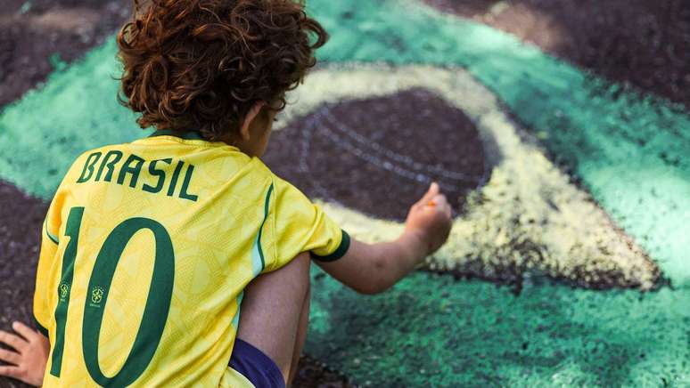 Crian&ccedil;a pinta a bandeira do Brasil na rua, parte da decora&ccedil;&atilde;o para Copa do Mundo