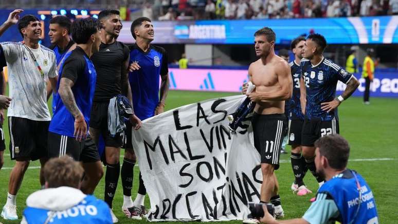 V&aacute;rios jogadores de futebol argentinos em um campo, segurando uma faixa com os dizeres "Las Malvinas Son Argentinas".