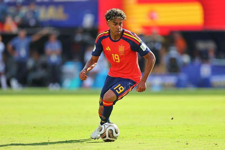 Lamine Yamal durante jogo da Espanha. Ele est&aacute; chutando a bola e com a camisa vermelha da sele&ccedil;&atilde;o.