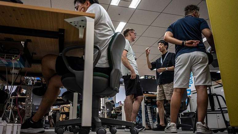 Quatro homens usando bermuda em um escrit&oacute;rio em T&oacute;quio, no Jap&atilde;o. Tr&ecirc;s deles est&atilde;o de p&eacute;, e um est&aacute; sentado com os cotovelos apoiados na mesa.