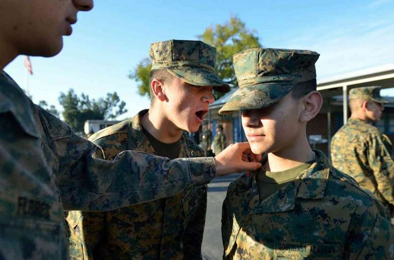 Meninos em uniforme parados do lado de fora, um com a m&atilde;o no ombro do outro, enquanto outro tem a boca aberta