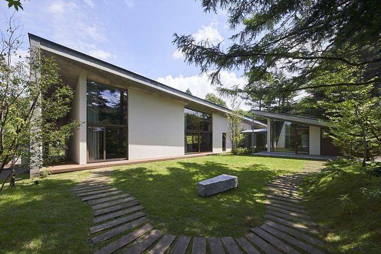 Casa t&eacute;rrea com anexo, em meio a um jardim arborizado em dia de sol