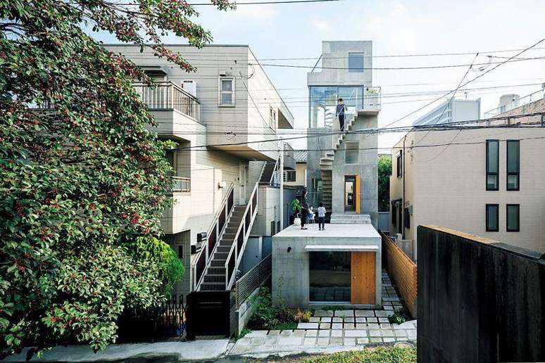 Casa com uma torre com escada externa em um terreno min&uacute;sculo, ao lado de outras constru&ccedil;&otilde;es no meio da cidade