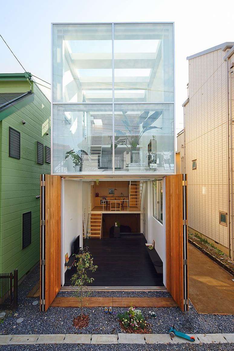 Casa com andar superior de vidro, entre duas constru&ccedil;&otilde;es vizinhas no meio da cidade