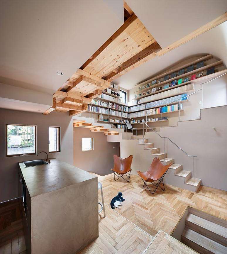 Casa repleta de escadas, com uma estante de livros e um gato deitado no ch&atilde;o de madeira