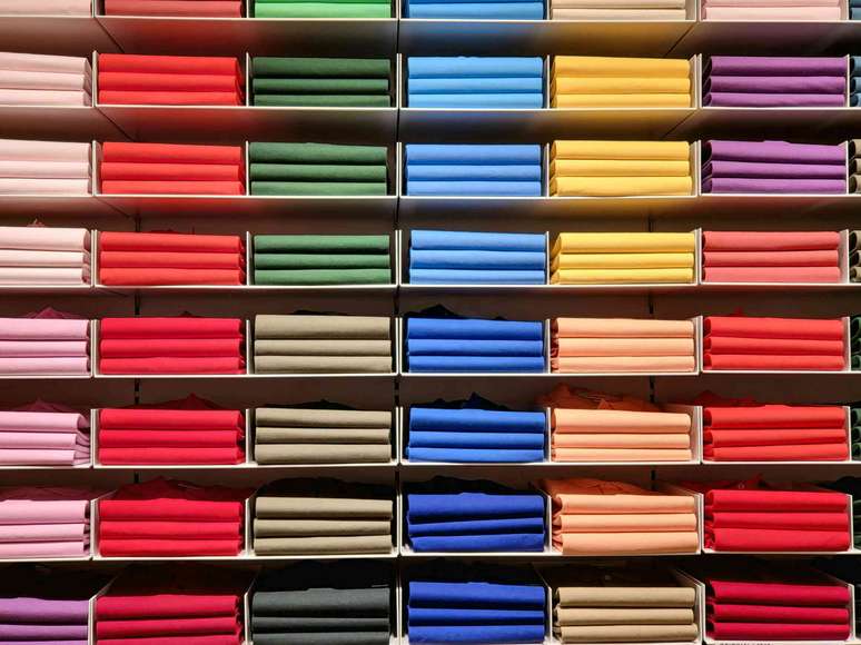 prateleiras cheias de pilhas de camisetas coloridas dobradas, rosa, vermelho, verde, azul, amarelo, roxo (da esquerda para a direita)