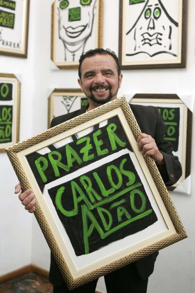 Carlos Ad&atilde;o segura quadro com seu nome em foto de 2010. Aposentado, conhecido por pintar seu nome por paredes da grande S&atilde;o Paulo, morreu em 8 de agosto de 2026.