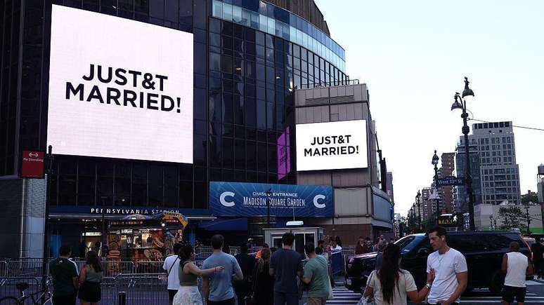 Pessoas assistem a tel&otilde;es gigantes exibindo a mensagem "JUST&T MARRIED!" (T&T de Taylor e Travis) do lado de fora do Madison Square Garden, local onde supostamente aconteceria a cerim&ocirc;nia de casamento da cantora pop Taylor Swift e do atleta profissional Travis Kelce, na cidade de Nova York, em 3 de julho de 2026.