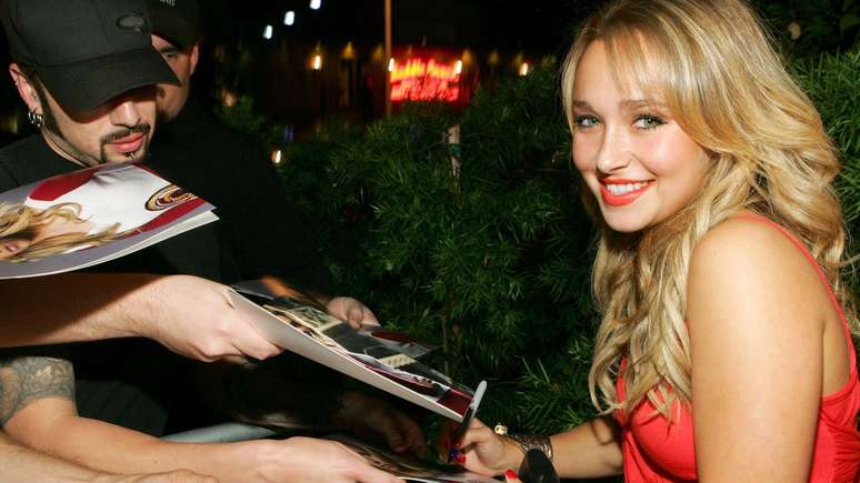 Hayden Panettiere no tapete vermelho da festa Teen Vogue Young Hollywood, distribuindo aut&oacute;grafos. Ela est&aacute; usando um vestido vermelho e sorrindo para a c&acirc;mera.