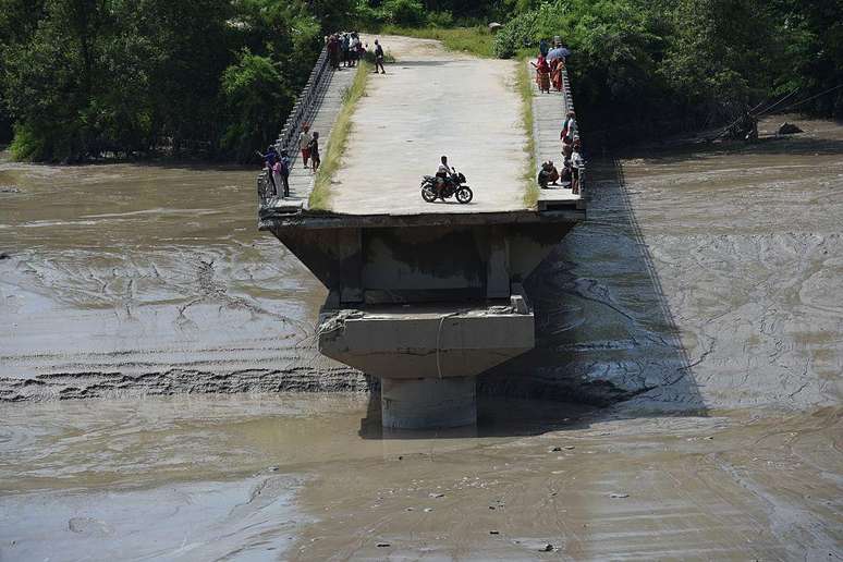 Um morador anda de motocicleta sobre os escombros de uma ponte levada pela enchente em Nuwakot, no Nepal, em 26 de agosto de 2026