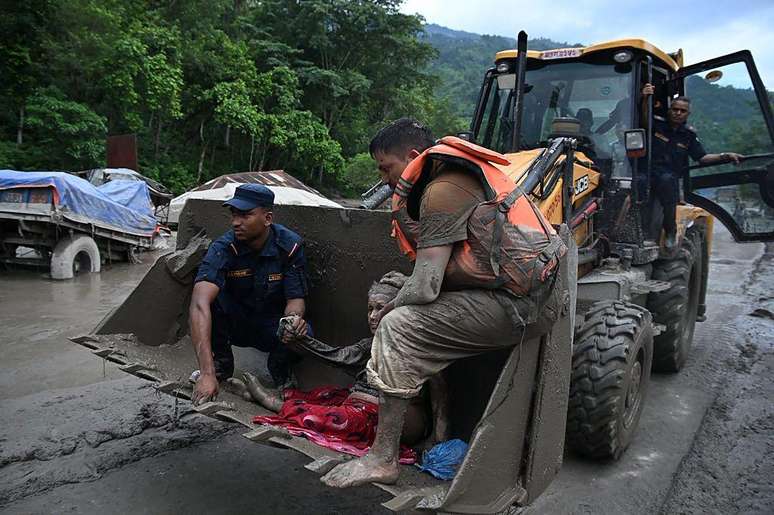 Equipes de resgate utilizam uma escavadeira para transportar uma pessoa afetada por enchentes repentinas em Devghat, no distrito de Nuwakot, no Nepal, em 26 de agosto de 2026