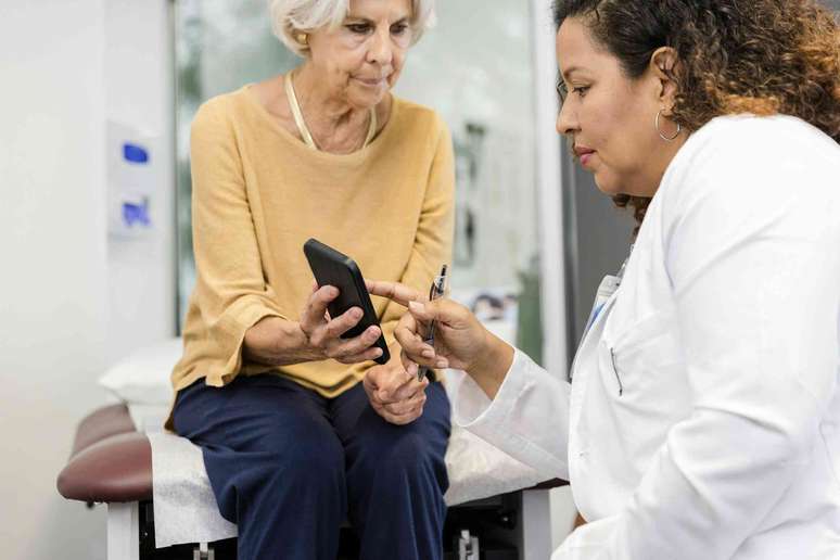 Paciente mostrando seu celular ao m&eacute;dico na sala de consulta