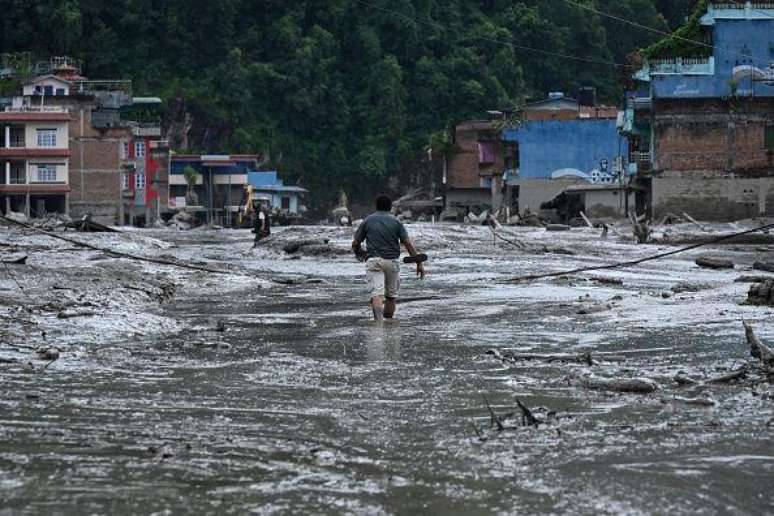 Um morador caminha por uma rua coberta de lama ap&oacute;s enchentes repentinas e um deslizamento de terra em Devighat, no distrito de Nuwakot, no Nepal, em 26 de agosto de 2026