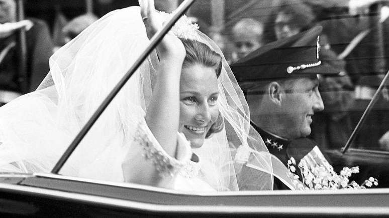 Uma fotografia tirada em 29 de agosto de 1968 mostra o pr&iacute;ncipe herdeiro da Noruega, Harald, e Sonja Haraldsen acenando enquanto saem de carro da Catedral de Oslo durante a cerim&ocirc;nia de casamento. 