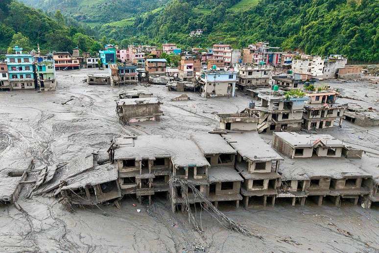 Casas cobertas de lama ao lado de um rio e, atr&aacute;s, casas coloridas que n&atilde;o sofreram os efeitos da avalanche