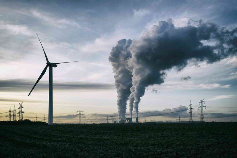 turbina e&oacute;lica e usina a carv&atilde;o vistas &agrave; dist&acirc;ncia, c&eacute;u cinza.