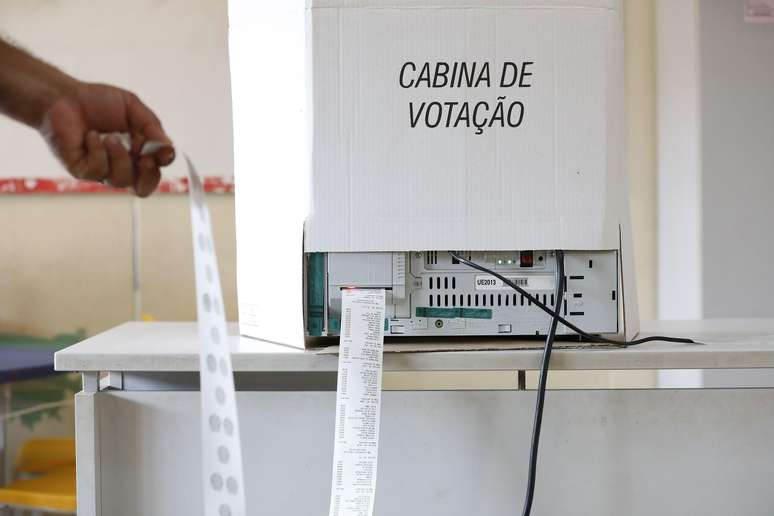 Boletim de urna eletr&ocirc;nica sendo impresso, uma m&atilde;o segura o papel que sai da urna