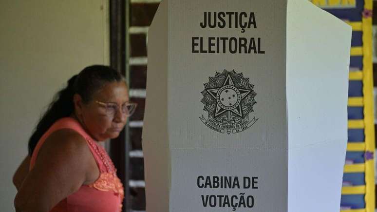 Cabina de vota&ccedil;&atilde;o da Justi&ccedil;a Eleitoral Brasileira, com mulher &agrave; frente, em imagem desfocada