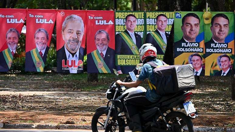Motoqueiro passa em frente a um varal de toalhas de Lula e Fl&aacute;vio Bolsonaro &agrave; venda. 