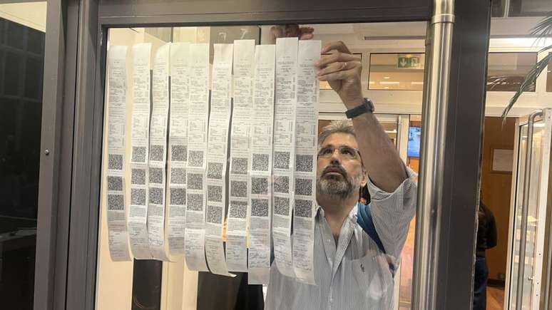 Mes&aacute;rios colam boletins de urna na frente do espa&ccedil;o de vota&ccedil;&atilde;o em Paris.