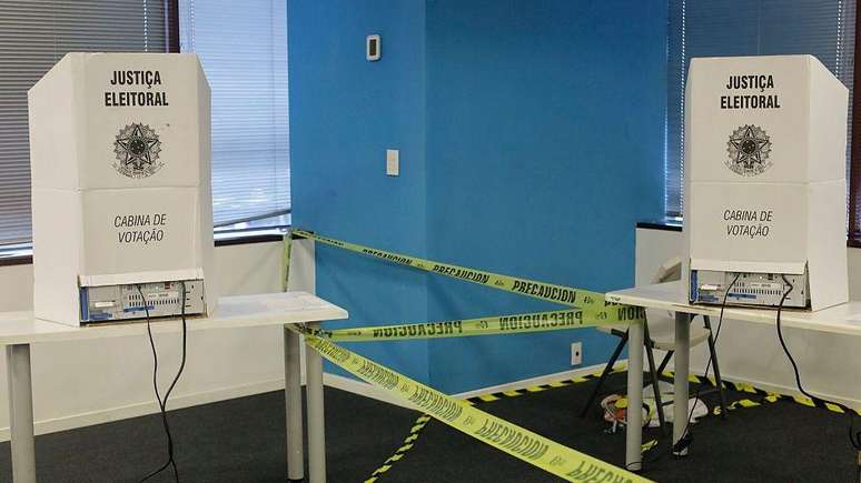 Cabines de vota&ccedil;&atilde;o isoladas por fitas de advert&ecirc;ncia em uma sala