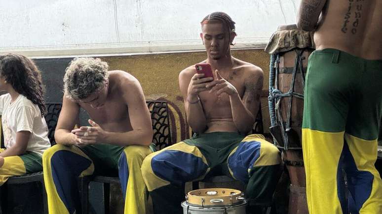 Samuel, ao centro, mexe no celular entre dois shows de capoeira na Laje Cultural da Rocinha, em 5 de outubro de 2026.