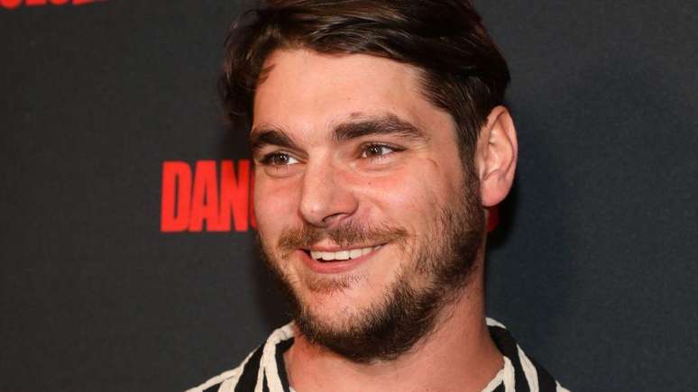 RJ Mitte participa de um evento de tapete vermelho em Los Angeles, em 2023. Ele est&aacute; sorrindo e tem barba.